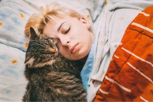 a blonde haired woman sleeping with a cat in bed