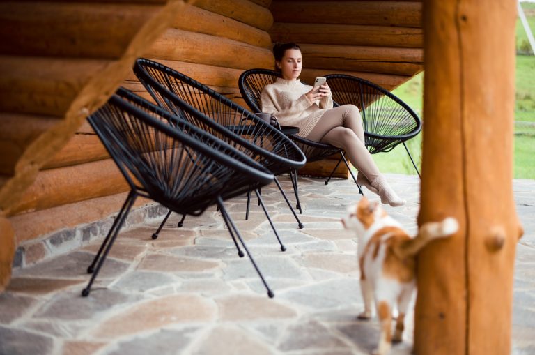 the woman sits outside in a chair while the cat follows her