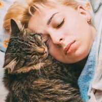 a blonde haired woman sleeping with a cat in bed