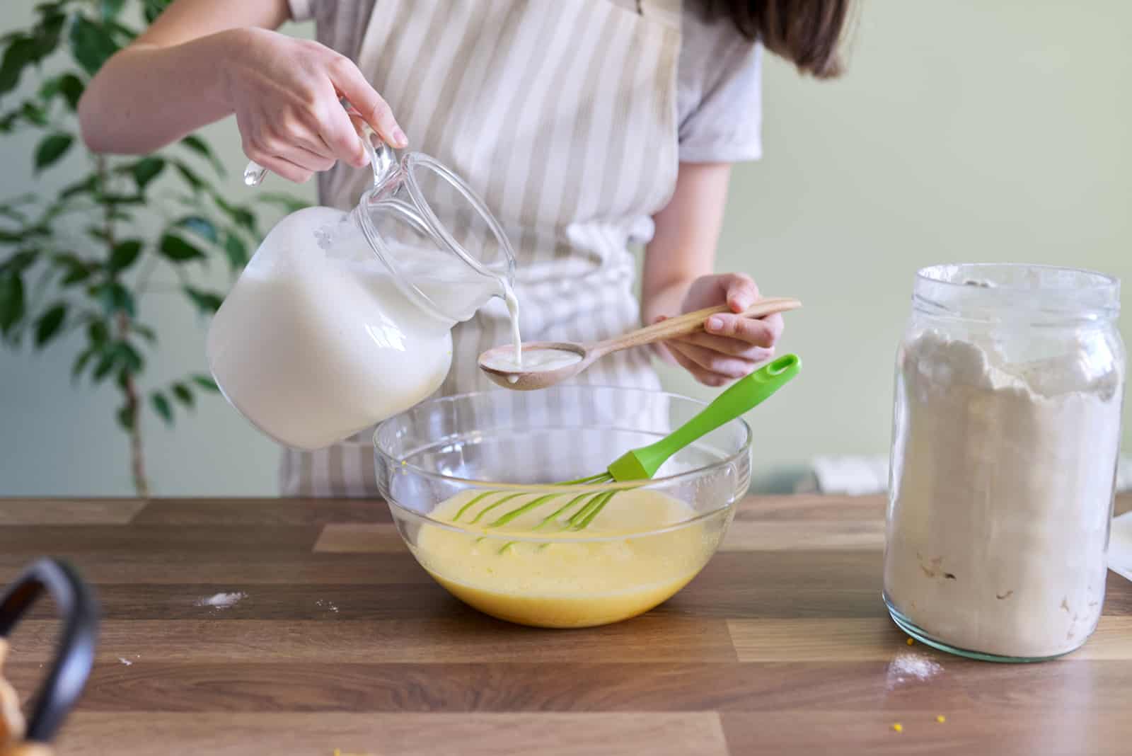 female hands pouring milk into a bowl with dough