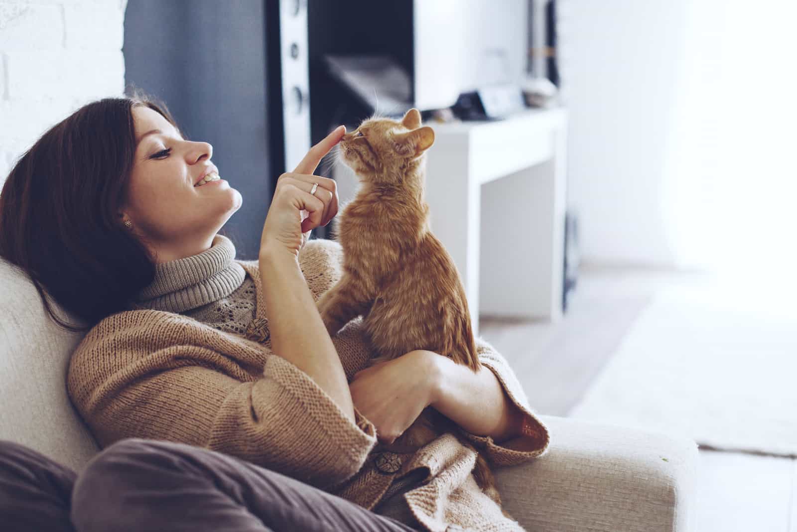 the woman sits on the couch and cuddles the cat