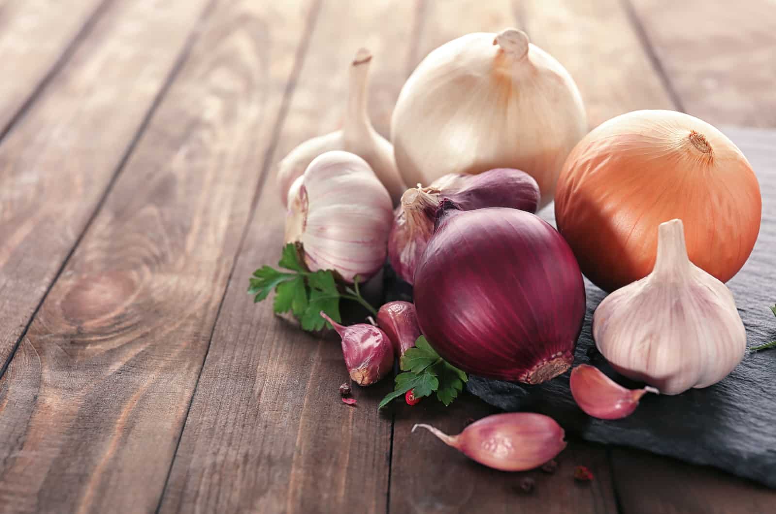 Slate plate with fresh garlic and onion on wooden table