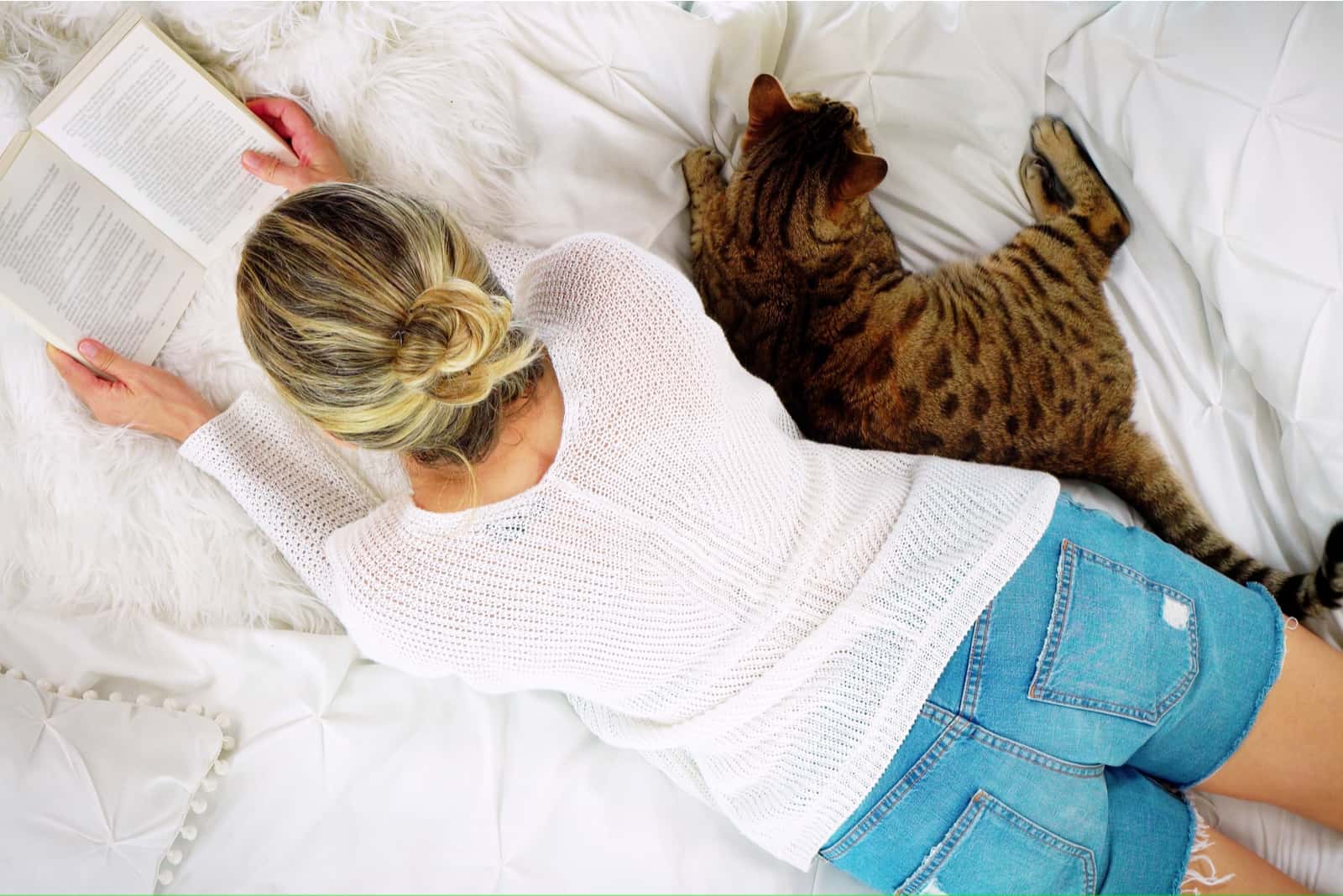 a woman lies with a cat and reads a book