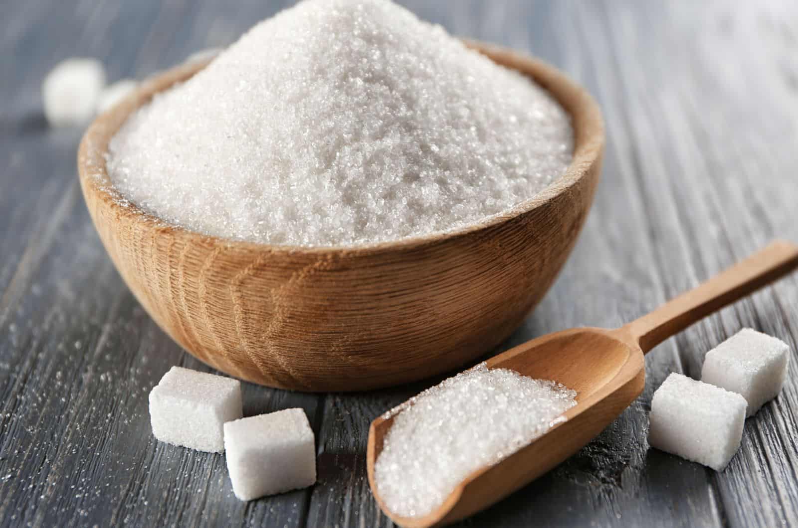 Bowl and scoop with white sand and lump sugar on wooden background