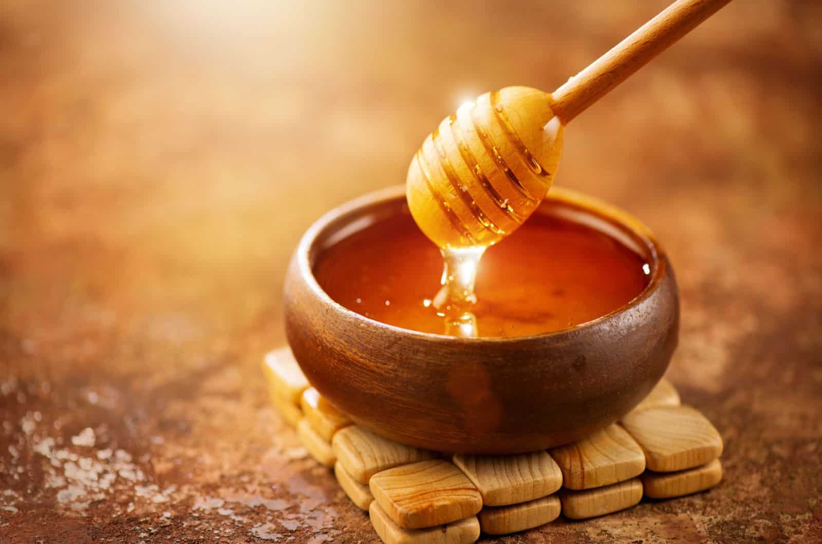 Honey dripping from honey dipper in wooden bowl
