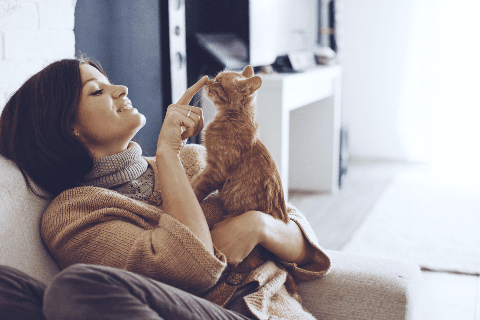 the woman sits on the couch and cuddles with the cat