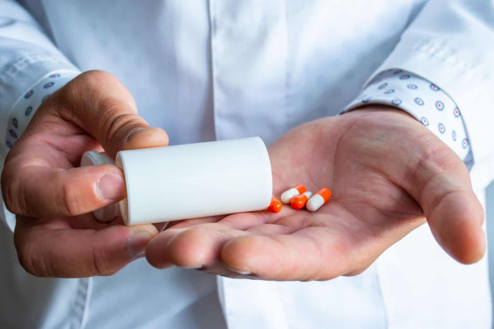 Doctor holds plastic container with orange capsules and pours them into other hand