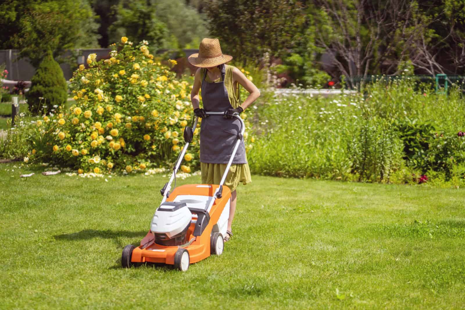 A young girl in a straw hat is mowing a lawn