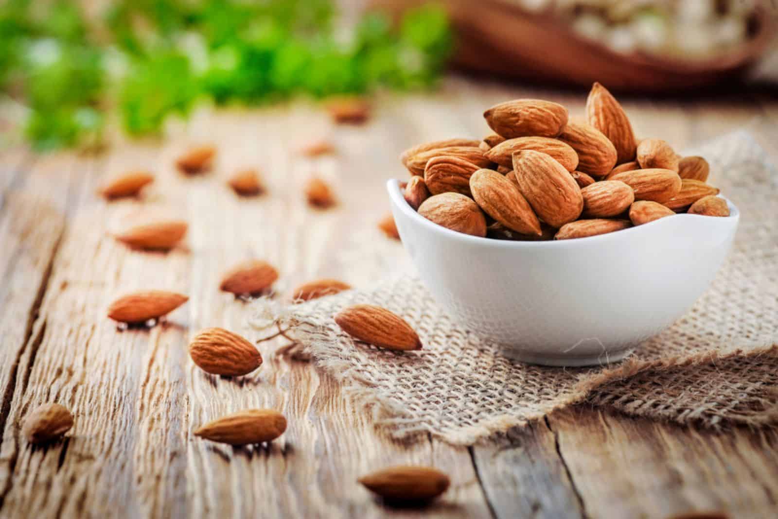 Almonds in white porcelain bowl on wooden table