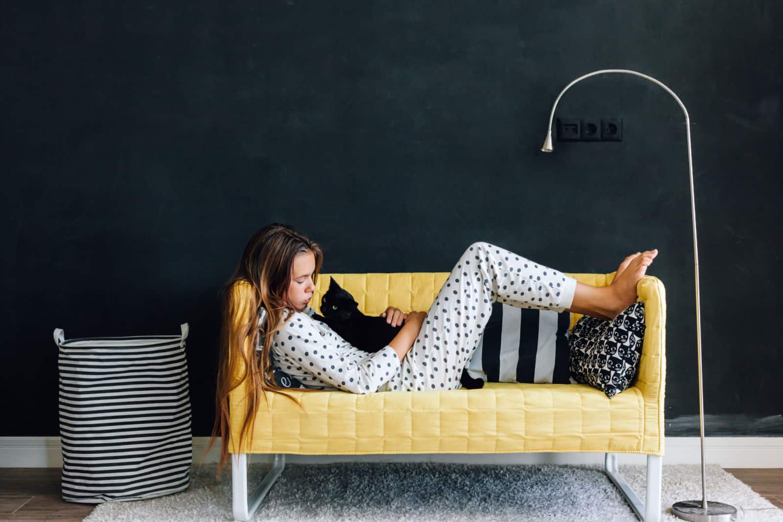 girl wearing pajama hugging her cat on the yellow couch