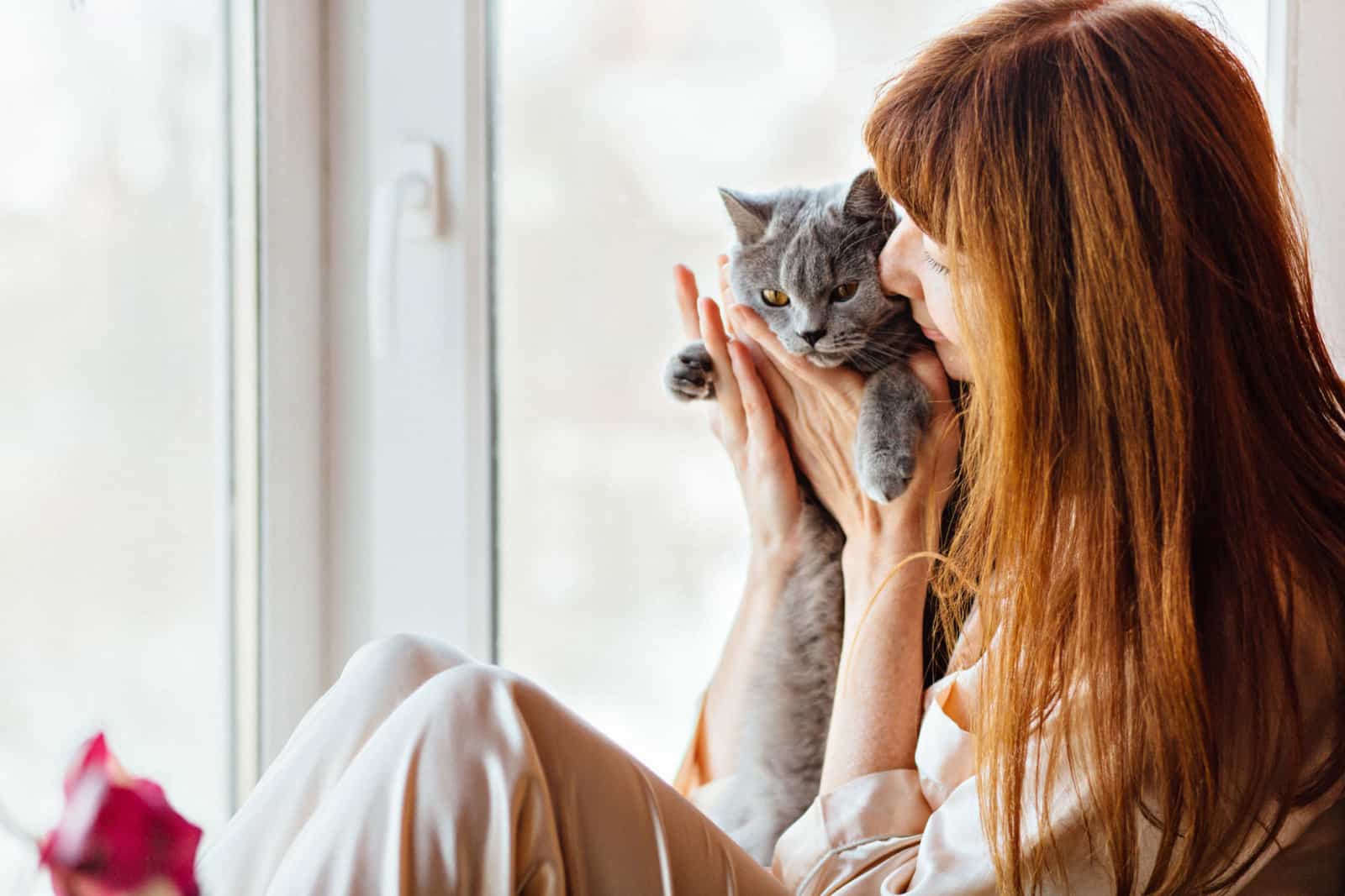 middle-aged redhead woman kissing gray cat