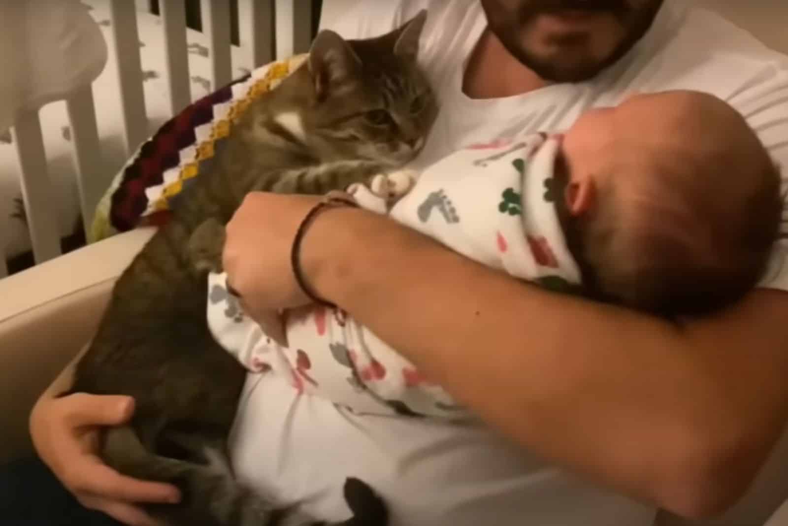 man holding cat and baby in arms