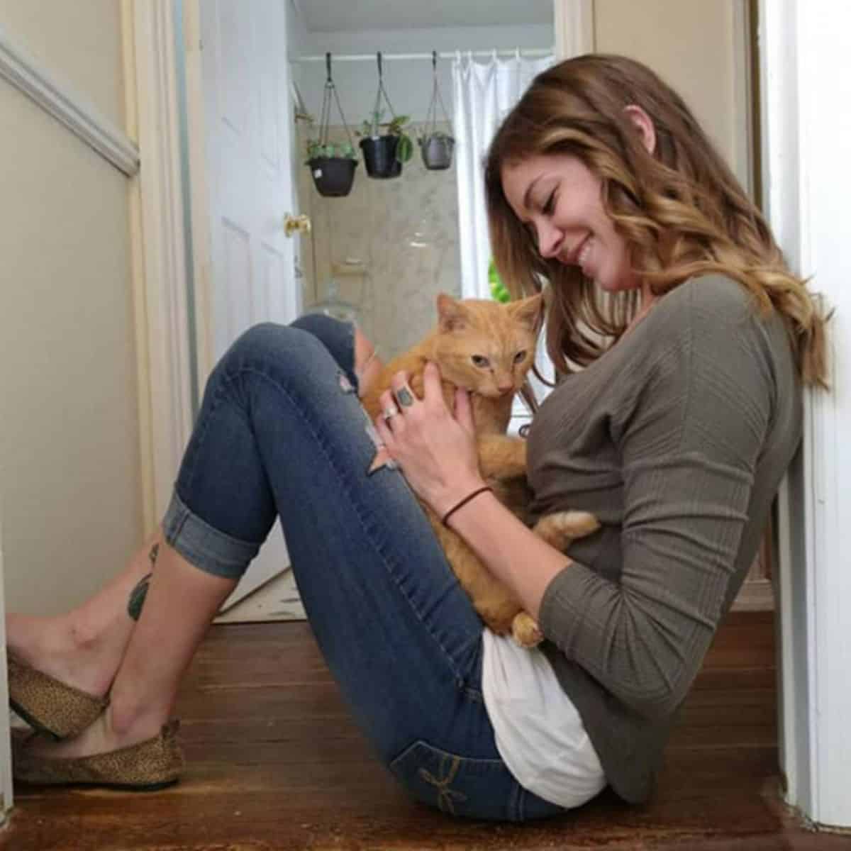 a smiling girl is sitting on the laminate floor and petting a cat