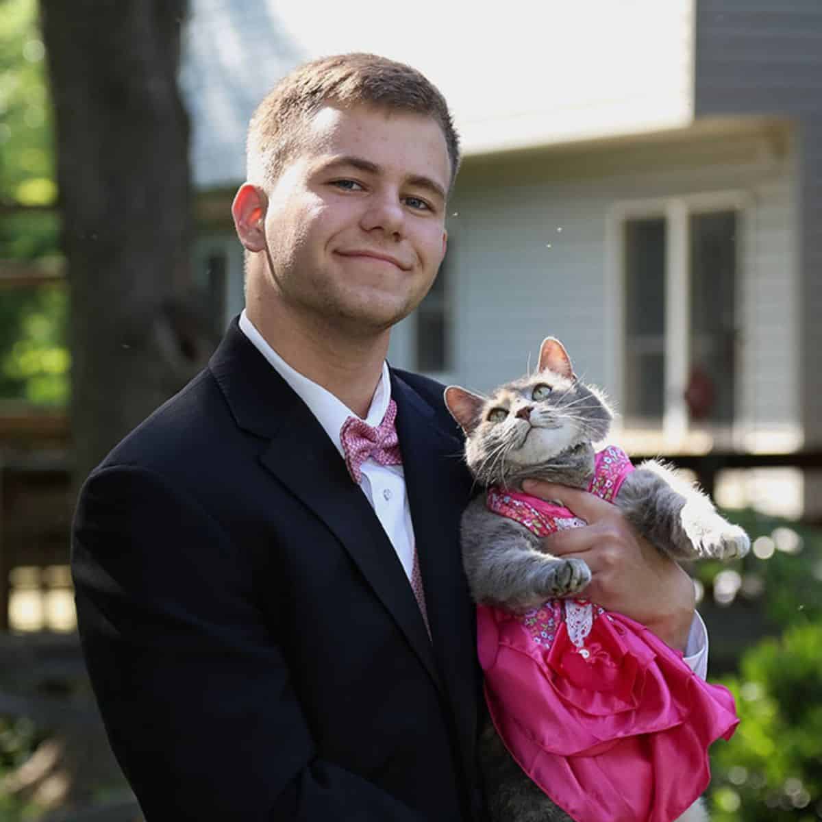 a man accompanied by a cat in his arms at the prom