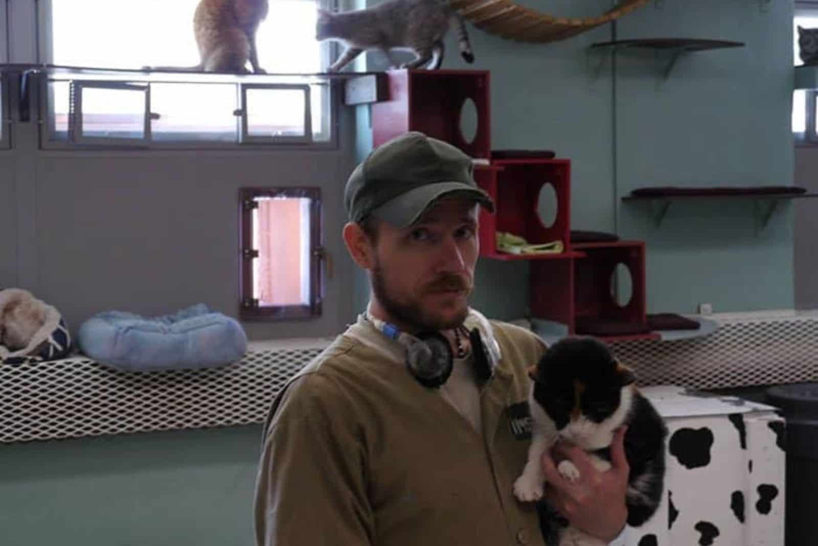 Guy holding a cat, while two cats trying to escape