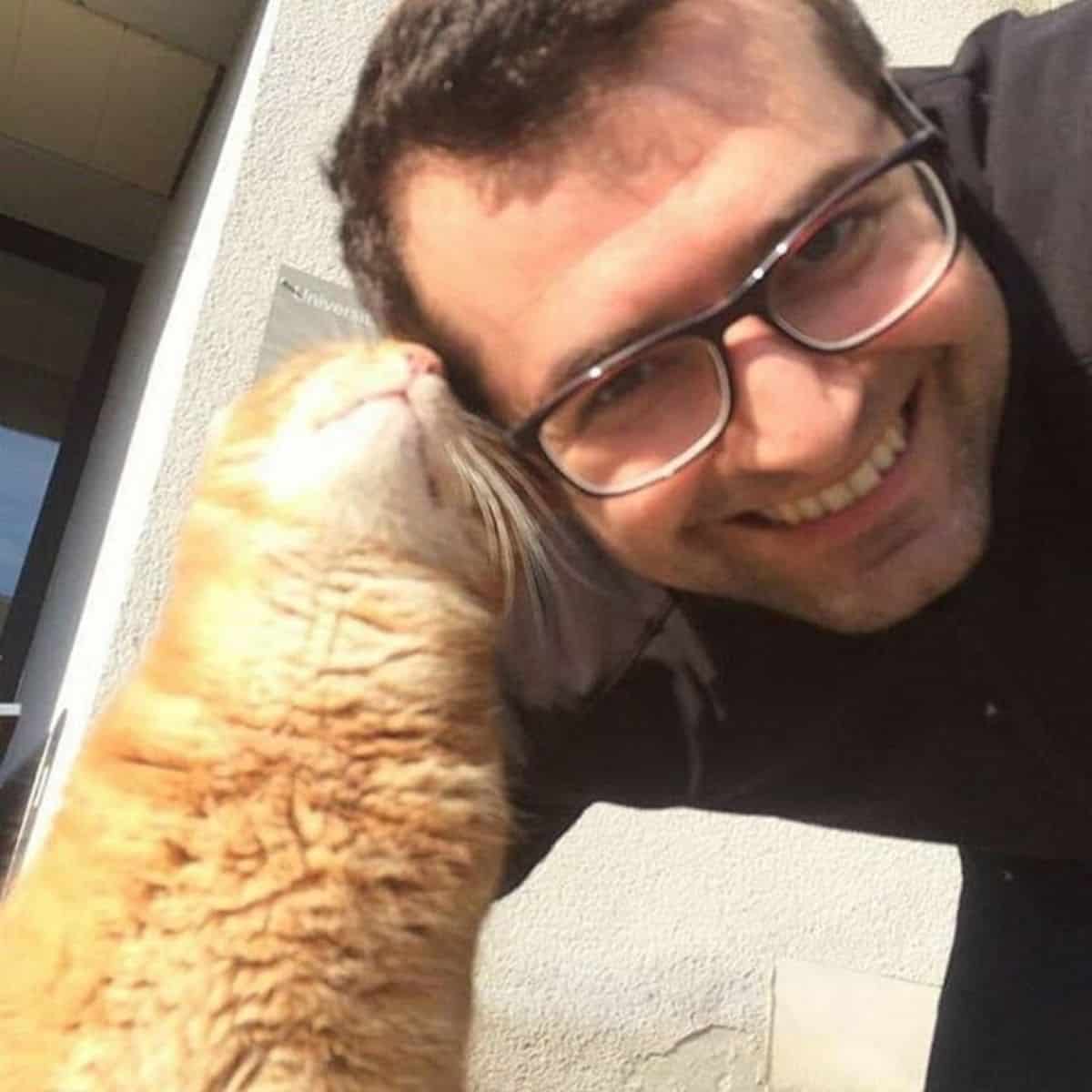 a smiling man with glasses cuddles with a cat
