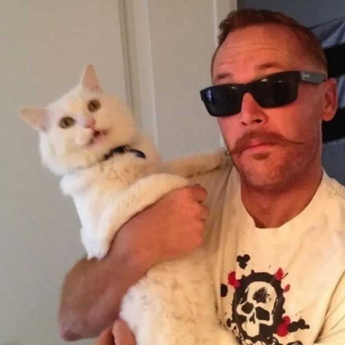 a man with glasses holds a white cat in his arms