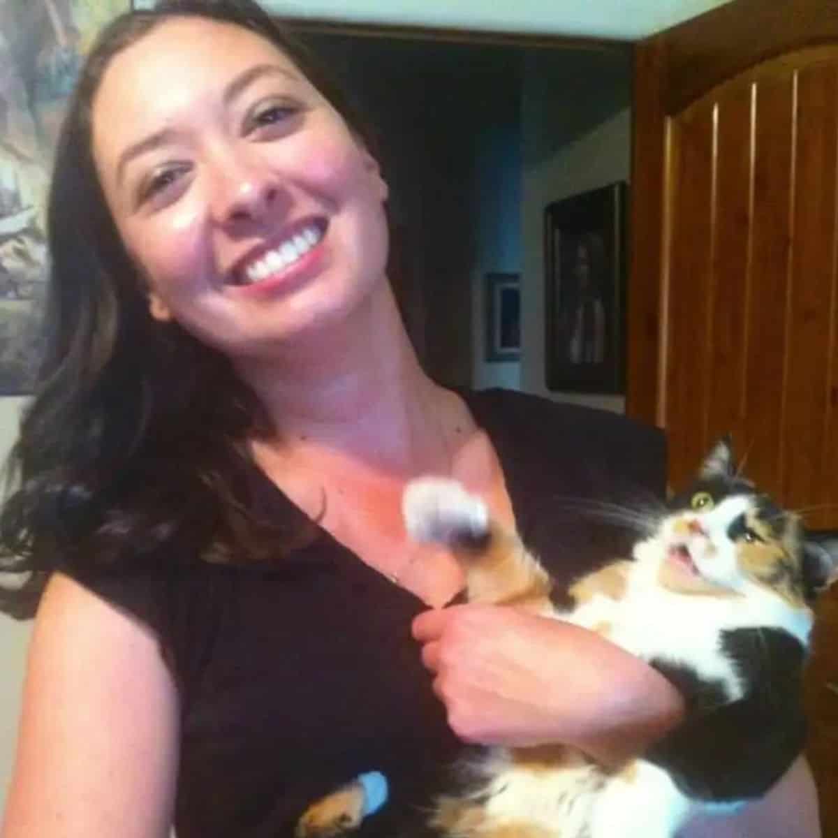 a smiling woman holds a grimacing cat