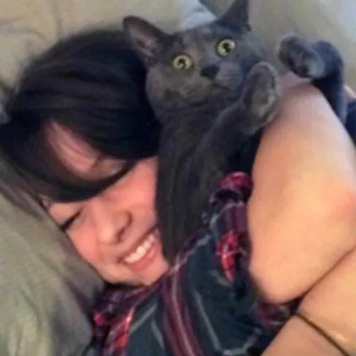 smiling woman hugs cat in bed