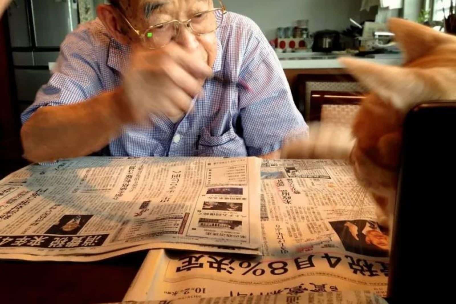man reading newspaper with cat on the table