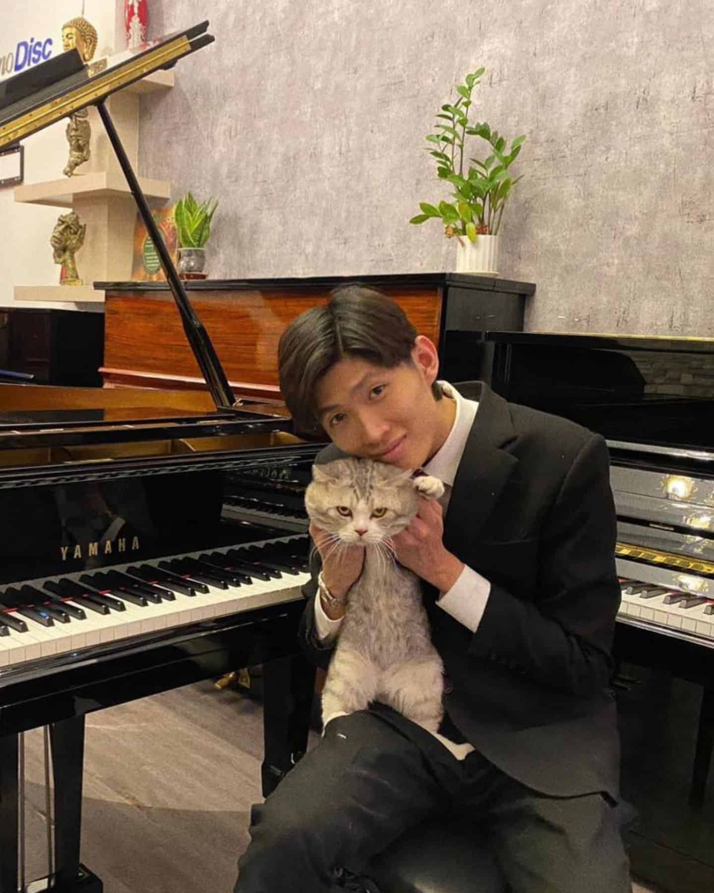 man holding cat and sitting by piano