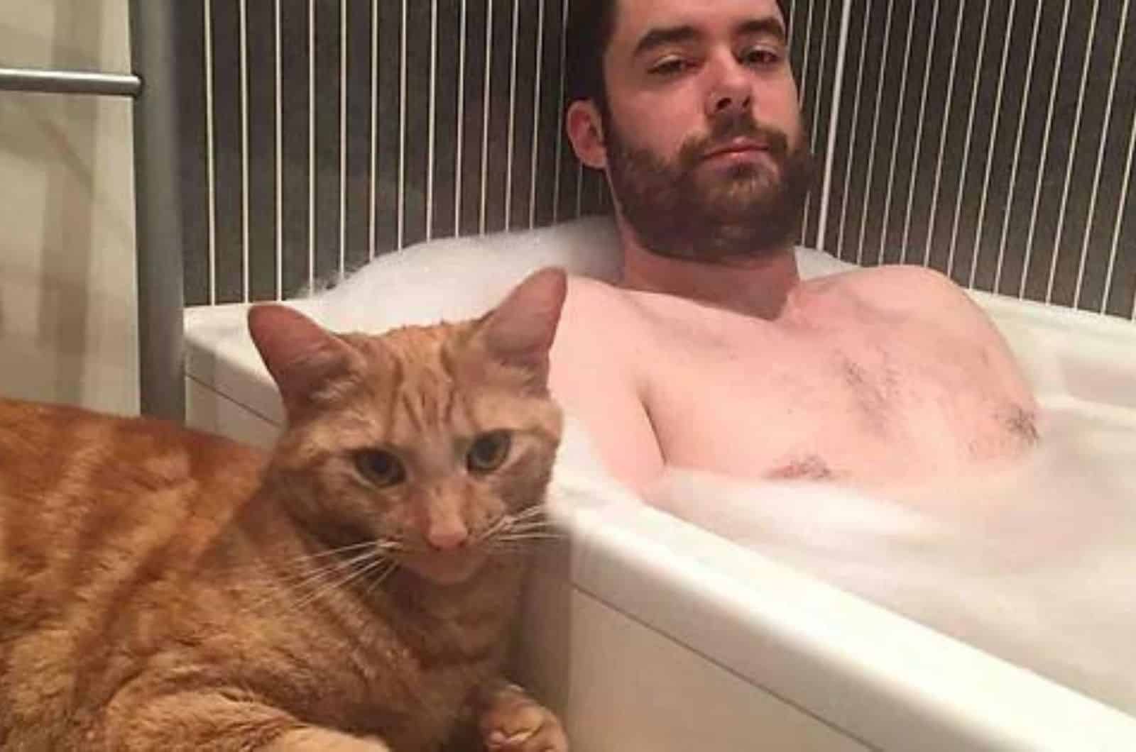 man taking a bath with cat next to him