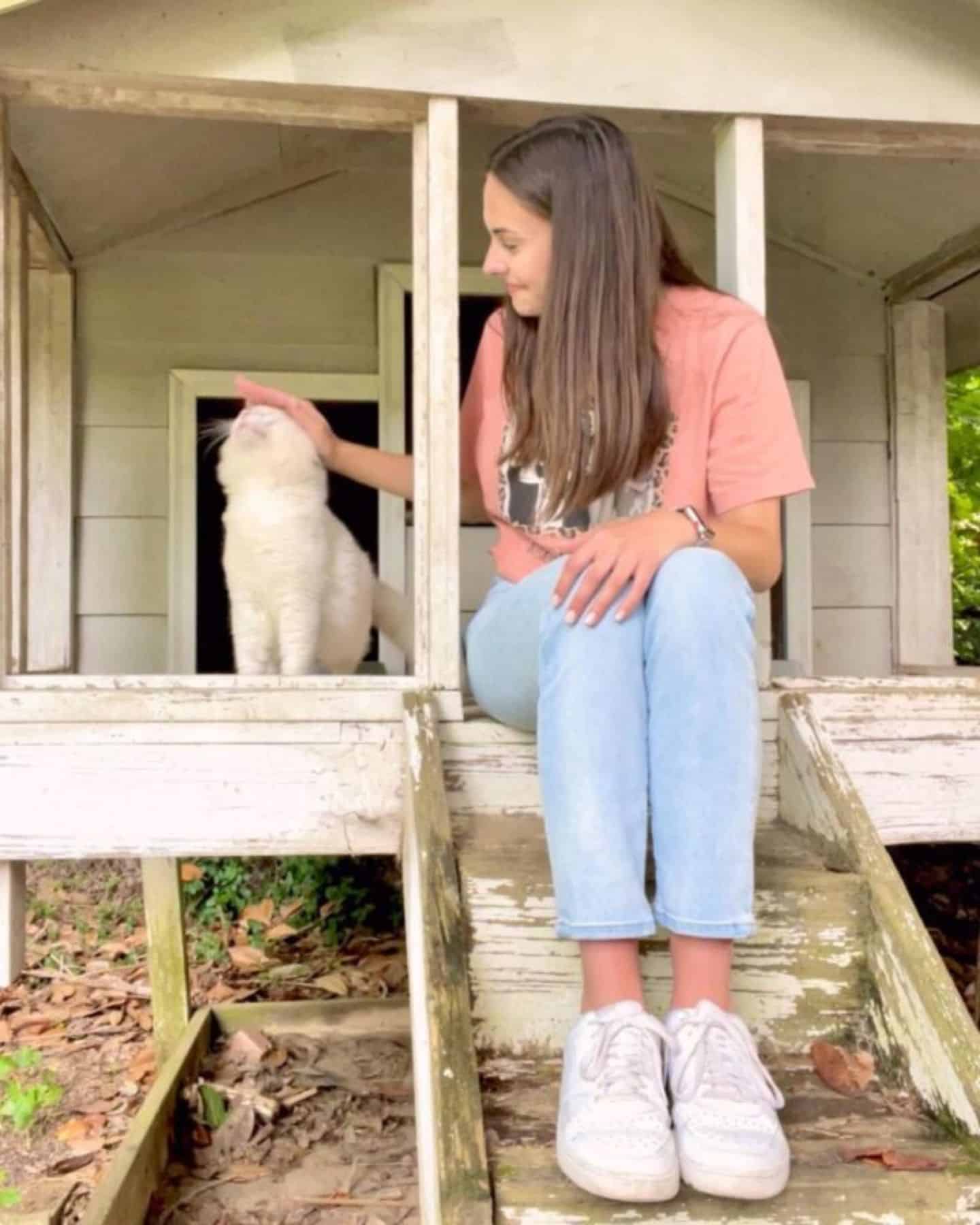 portrait of a girl sitting on wooden steps and petting a cat