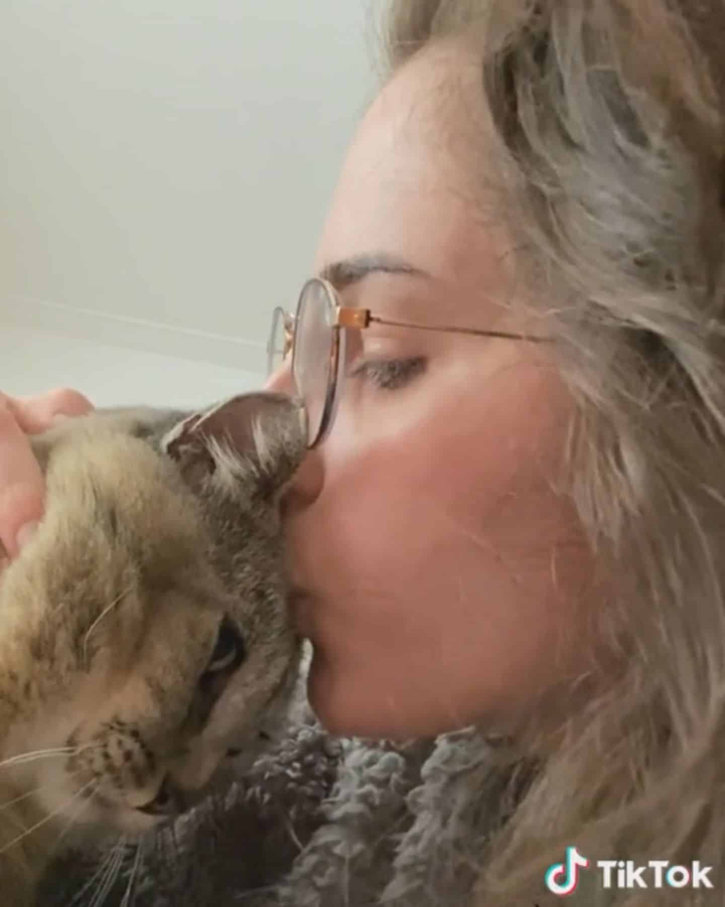 woman with glasses kissing a cat