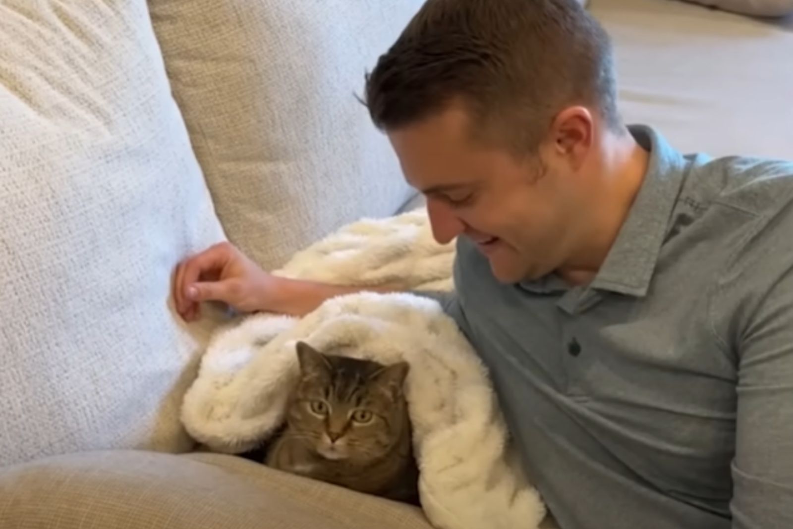 man looking at cat covered in blanket