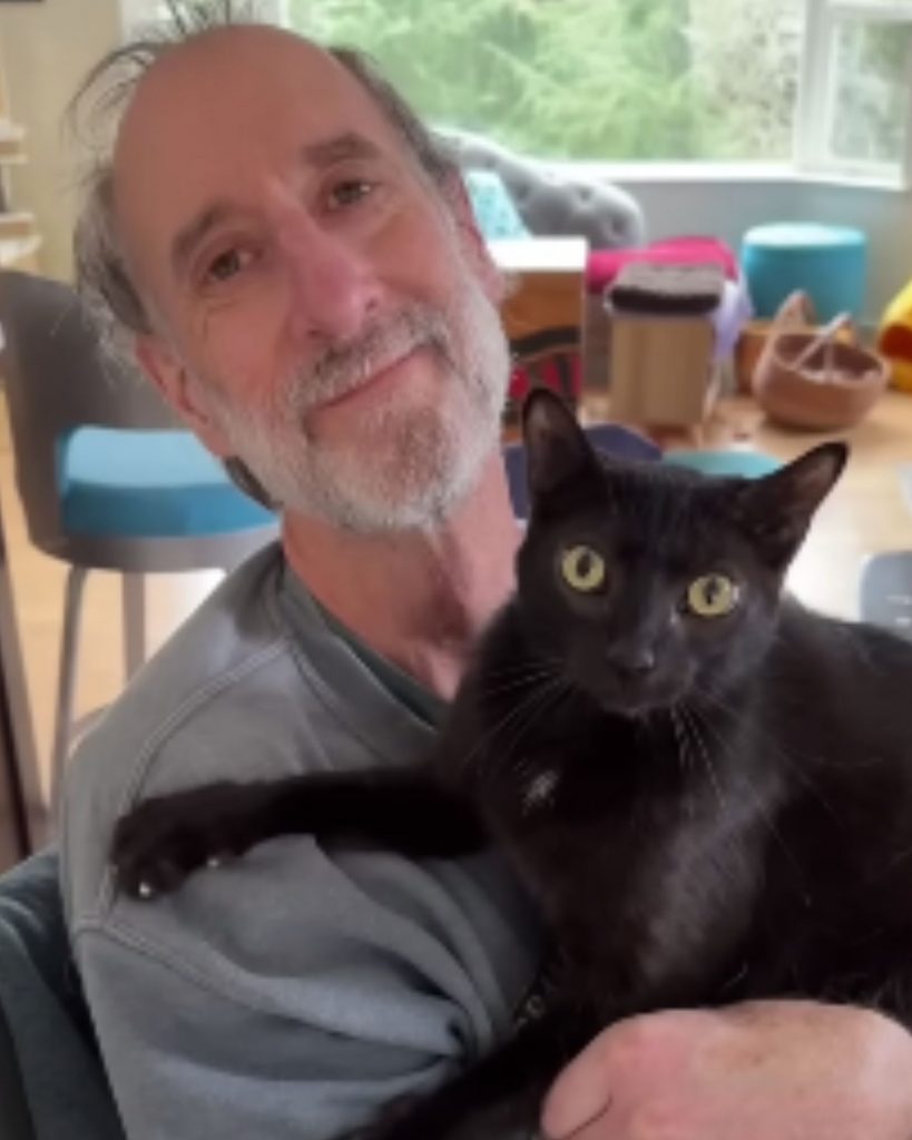 a smiling man holds a black cat in his arms