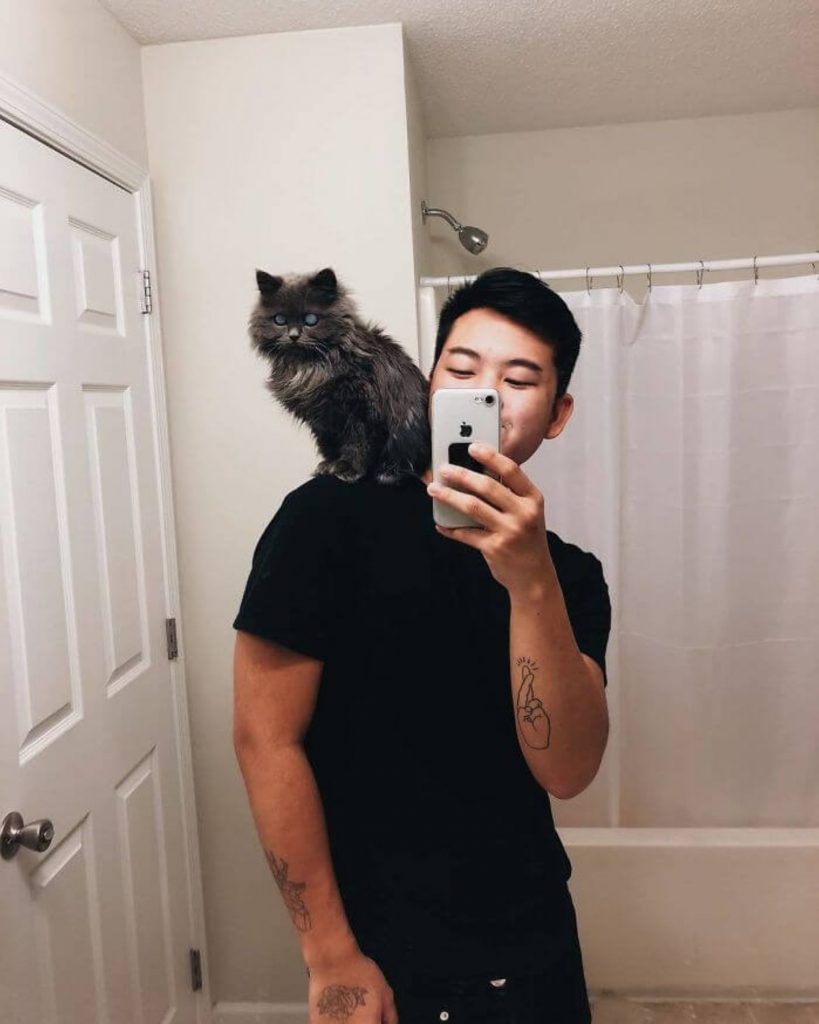 a Siamese cat sits on a man's shoulder while taking a picture