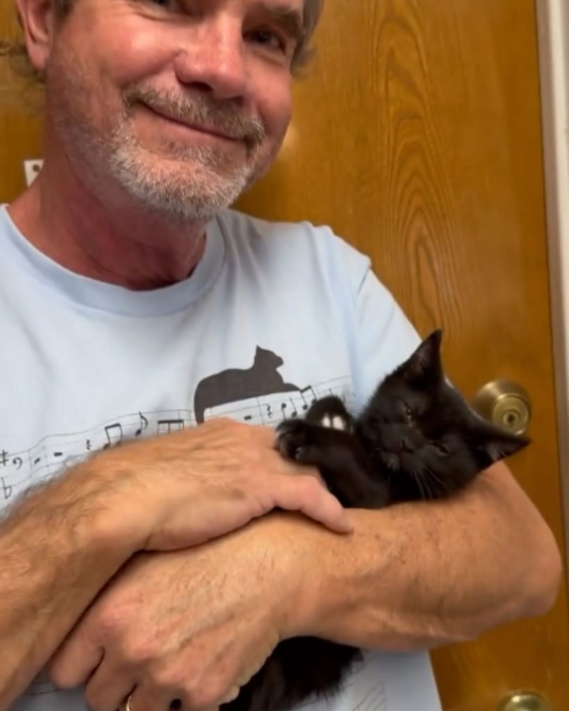 a man is holding a black kitten in his arms