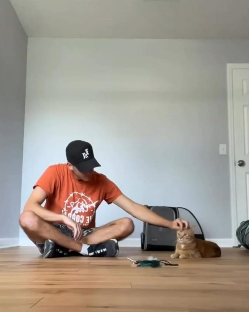 a man sits with a cat on the floor and pets it