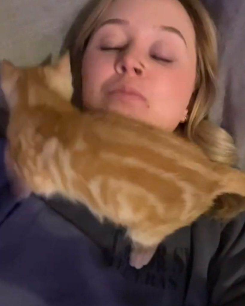 The girl is sleeping, the cat is walking around her neck