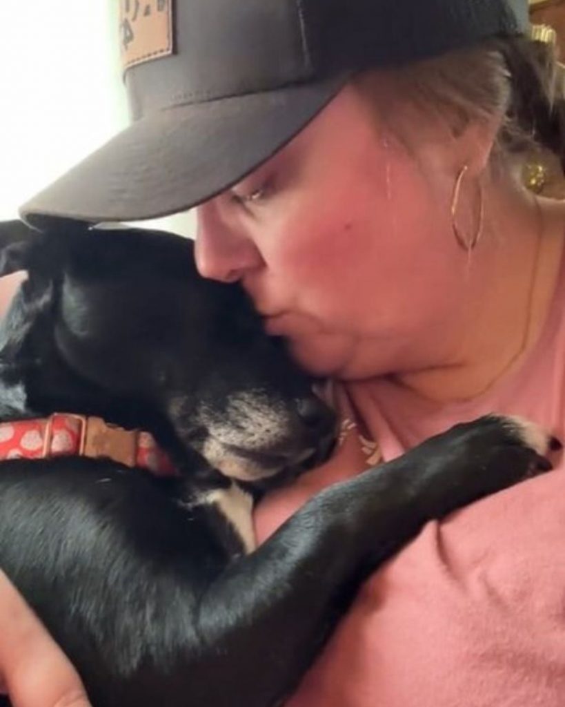 woman kissing a black dog