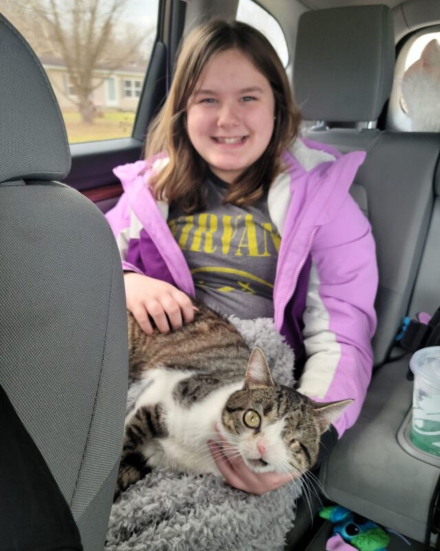 girl keeps a one-eyed cat on her lap in the car