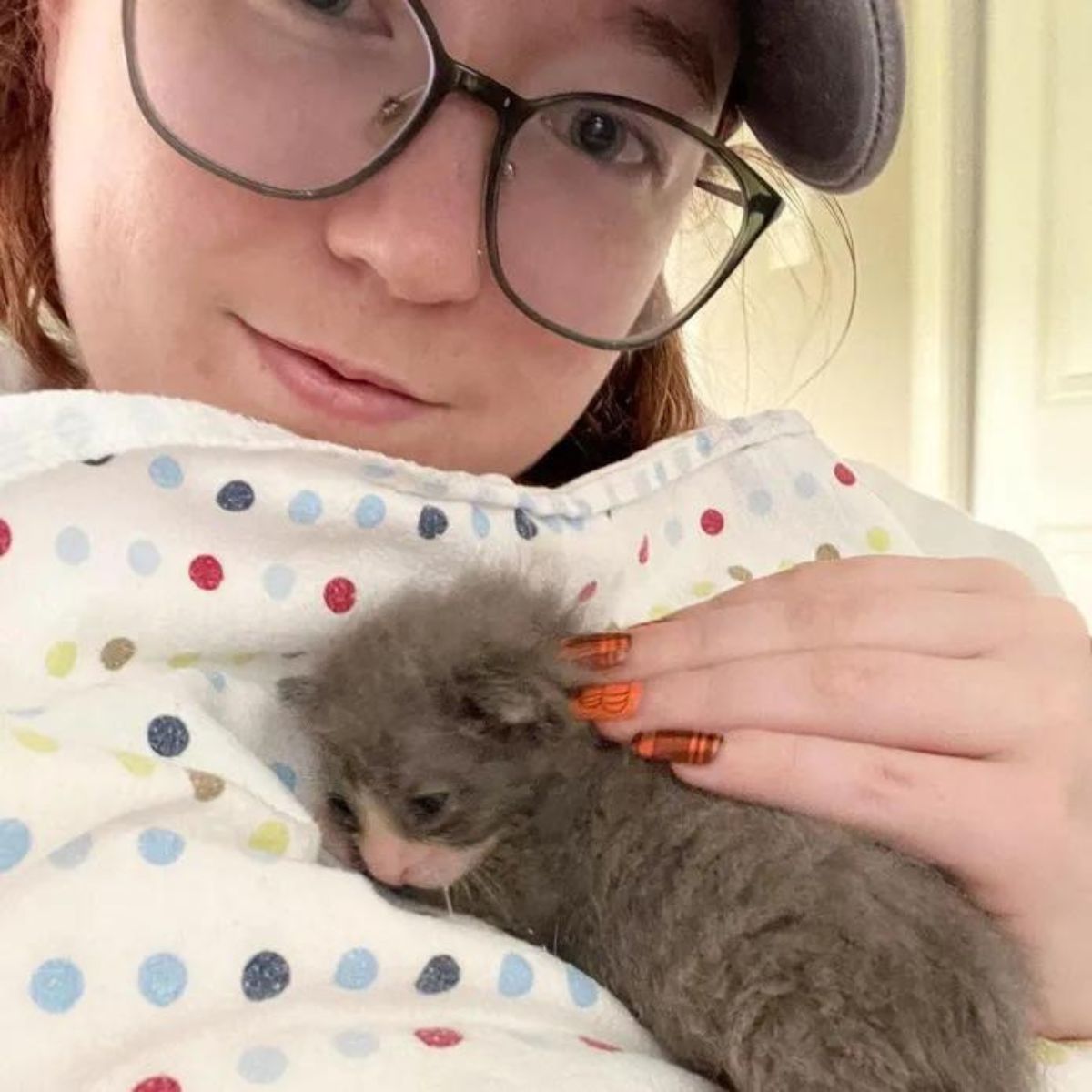 small kitten is lying on a blanket on a woman's chest
