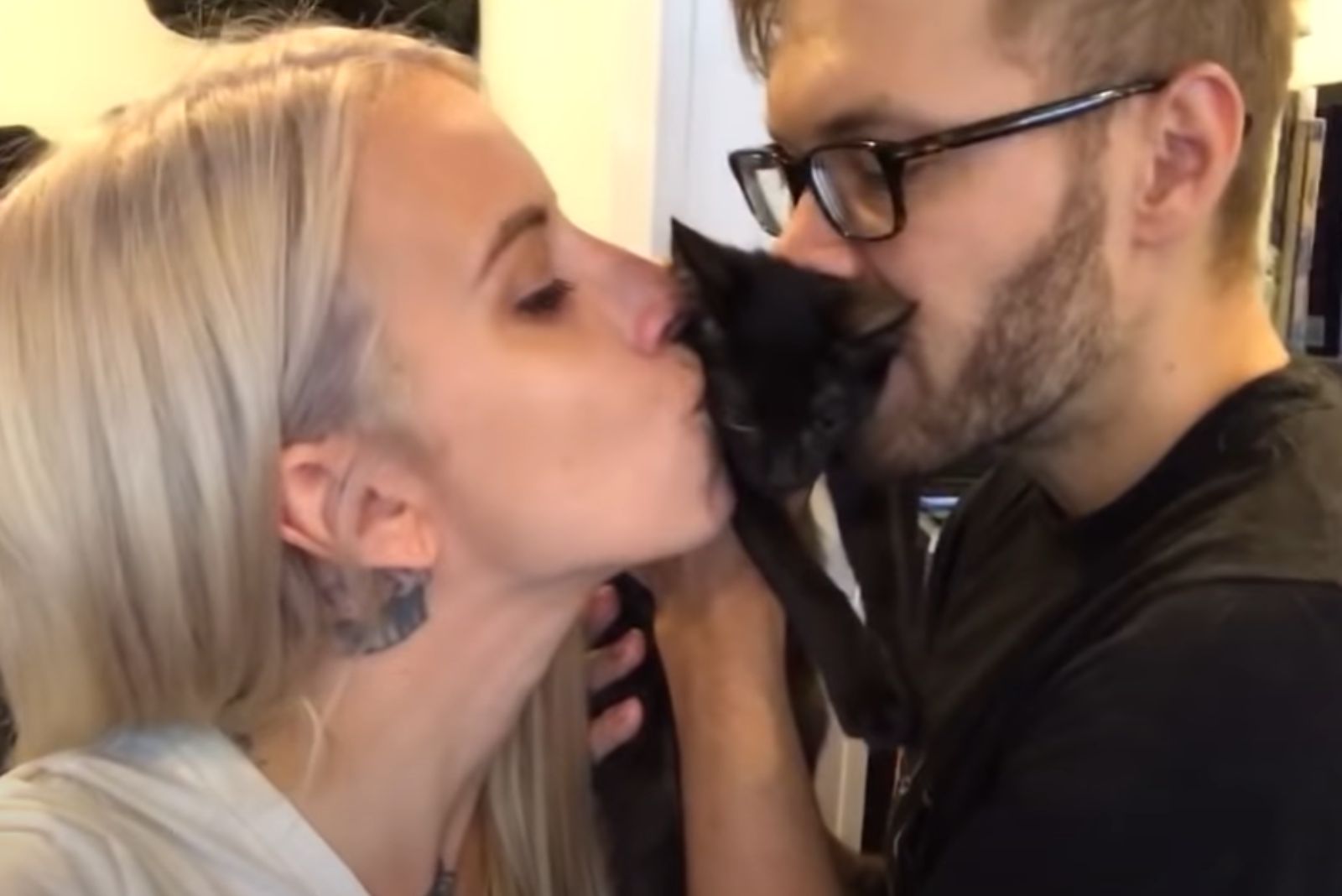man and a woman kiss a black kitten