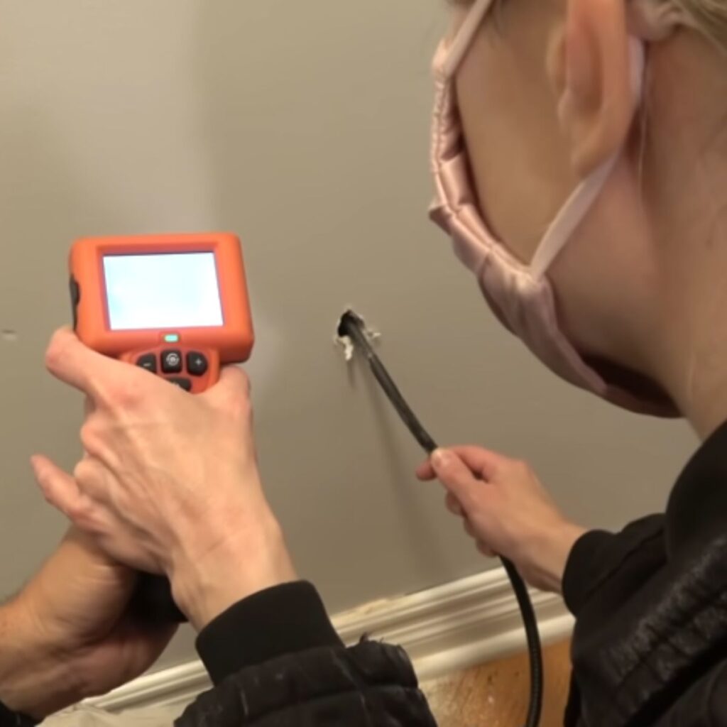 A man with a device checks for sounds in the wall