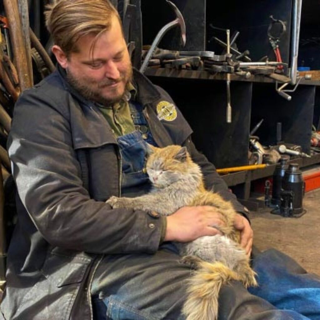 The worker is holding a cat in his lap