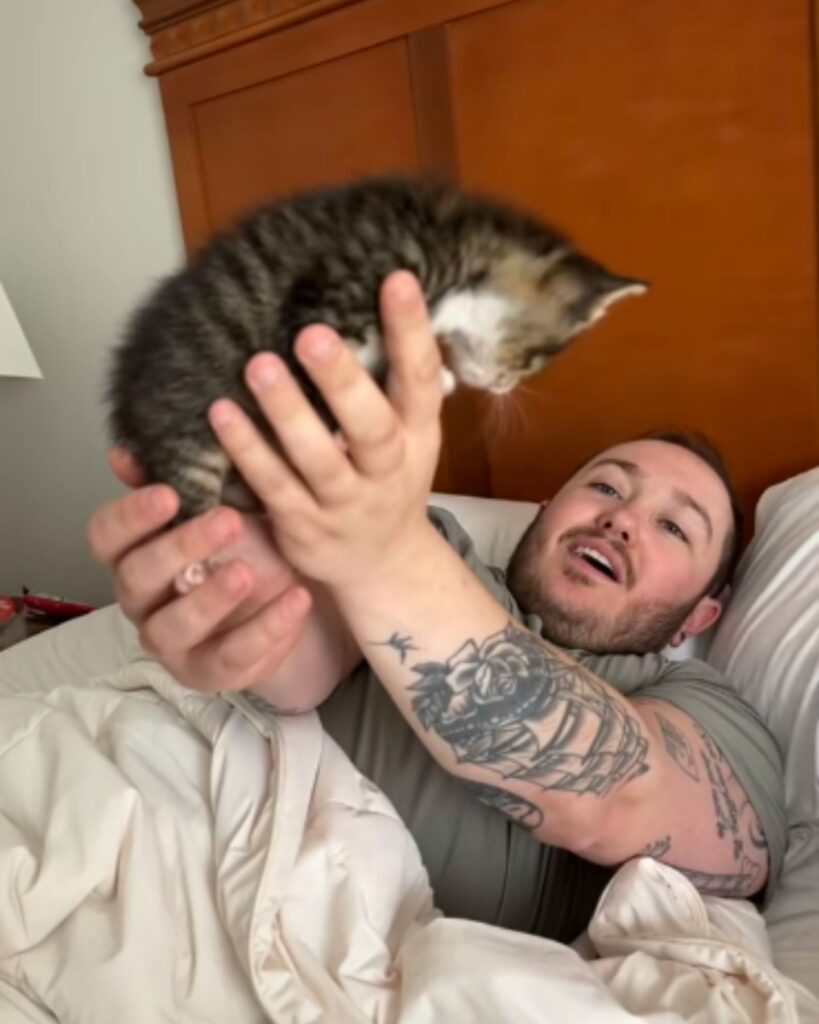 A man lies in bed and holds a kitten