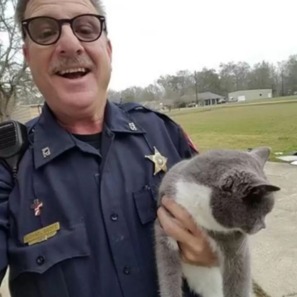 A police officer is holding a cat in his hands