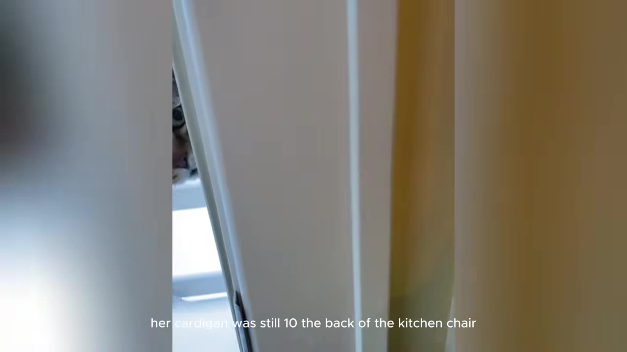 A tabby cat peeks out from behind a white door frame in a quiet house.
