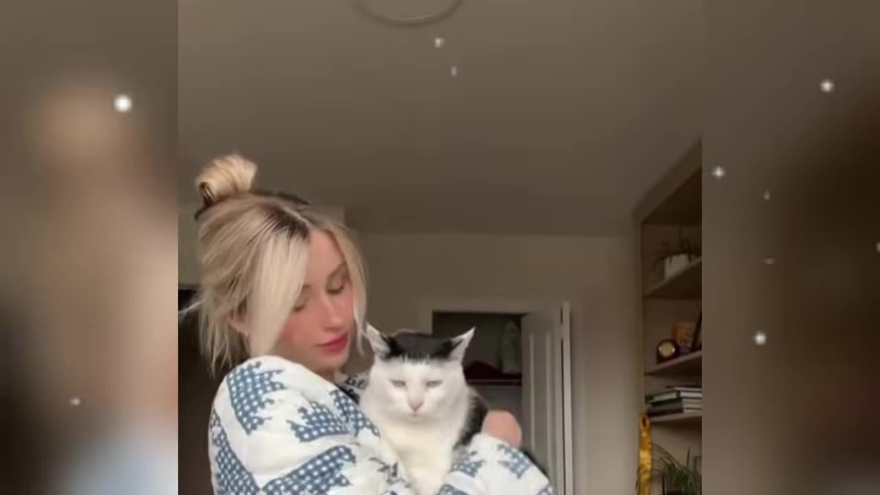 A blonde woman in a patterned sweater holds a black and white cat with a calm expression.