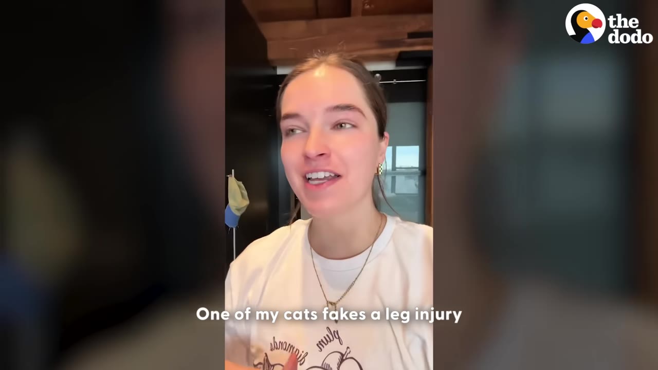 A woman in a white t-shirt looks at the camera with a caption that reads, 'One of my cats fakes a leg injury.'