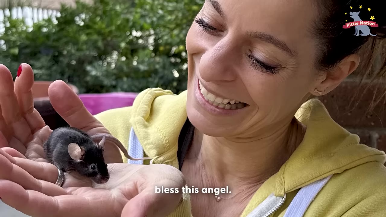 A close-up of a smiling woman holding a tiny, dark-furred mouse in her cupped hands.