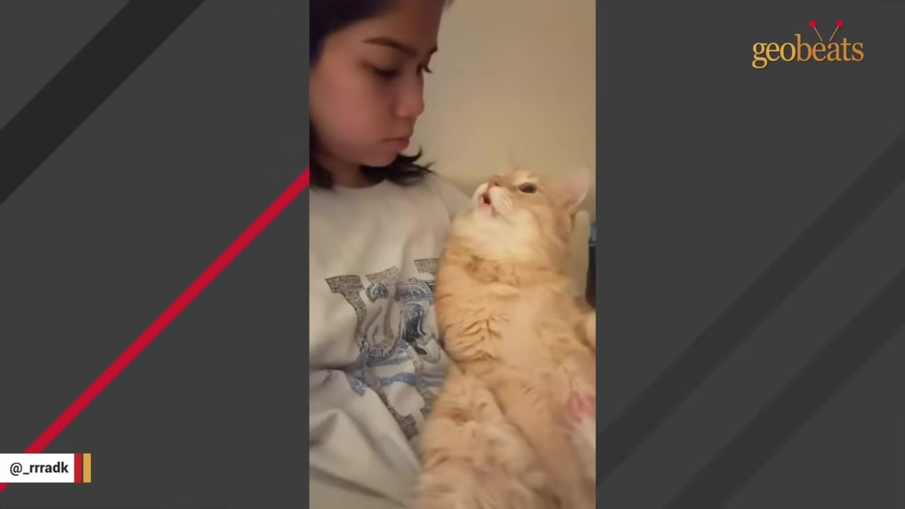 A young woman cradles an orange tabby cat in her arms as they look at each other.