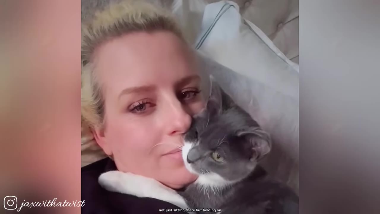 A close-up of a grey and white kitten cuddling closely against a woman's cheek as they lie down together.