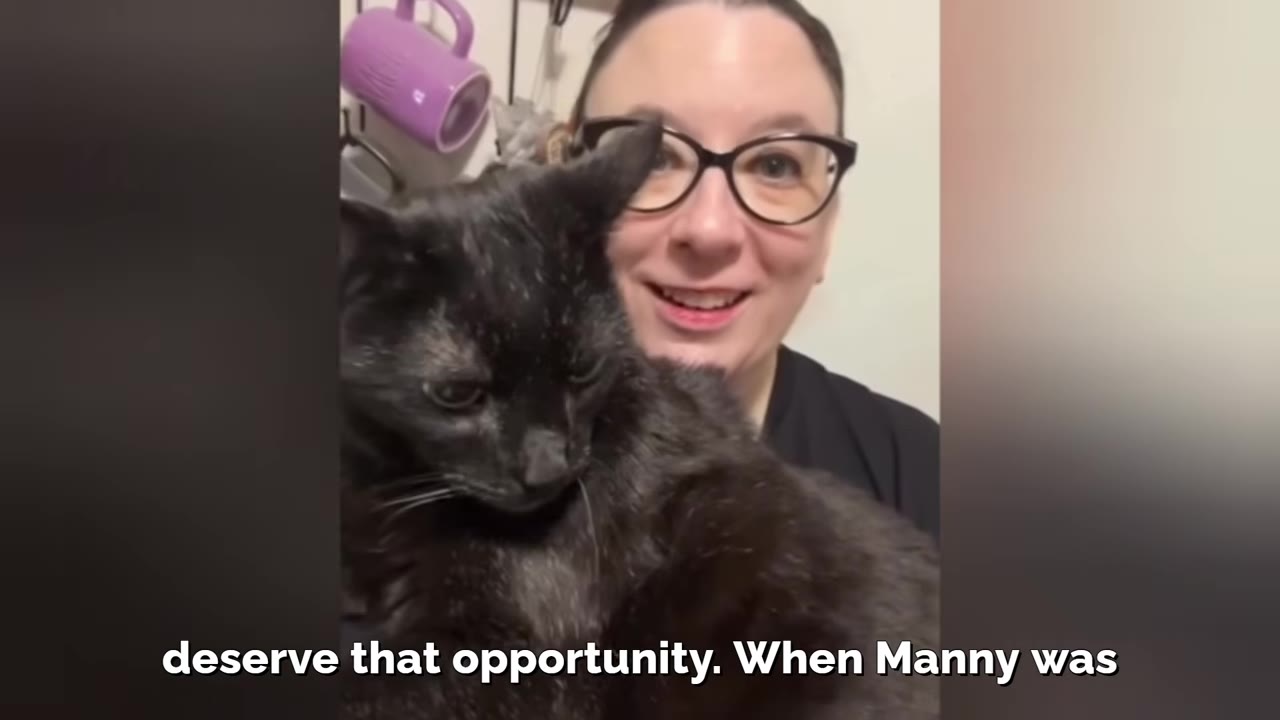 A smiling woman with glasses holds a black cat close to her chest.