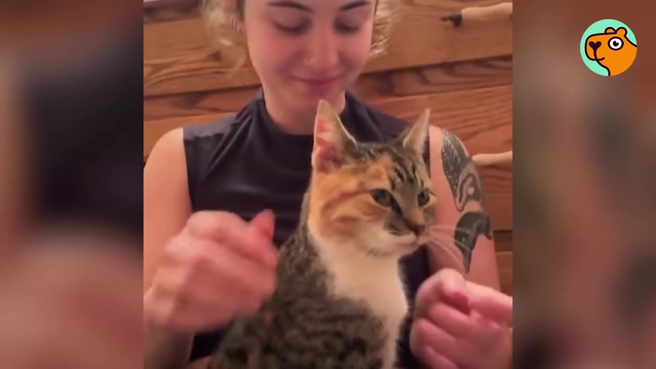 A smiling woman with a tattoo on her arm holds a calico cat in her lap.